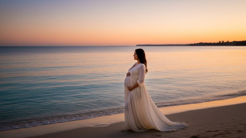 A radiant pregnant woman in a flowing white gown, silhouetted against a dramatic sunset over the turquoise waters of Safety Beach, showcasing the serene beauty of Coastal Maternity Photography Mount Martha Victoria.