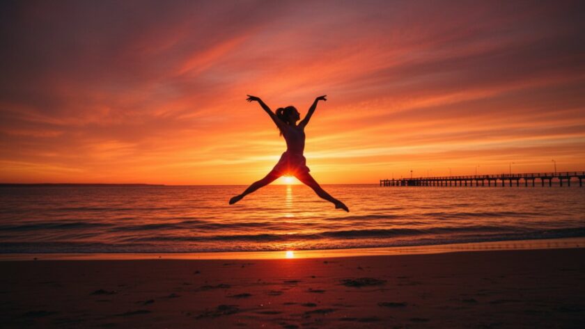 A ballet dancer striking an elegant, powerful pose mid-air during a dynamic dance photography Tootgarook beach sunset session, with the golden hour light illuminating their silhouette against the calm waters of Port Phillip Bay and the iconic Tootgarook pier in the distance, capturing an epic moment of grace and strength.