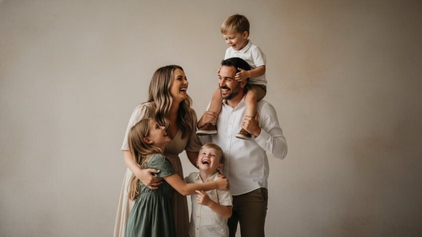 A vibrant family of four laughing joyfully during a bespoke studio photography session in Emerald, Victoria. The parents embrace their two young children, bathed in soft, professional lighting, capturing an authentic, 'epic moment' of connection. The image highlights the warm and inviting atmosphere of Emerald Victoria boutique studio photography for families.