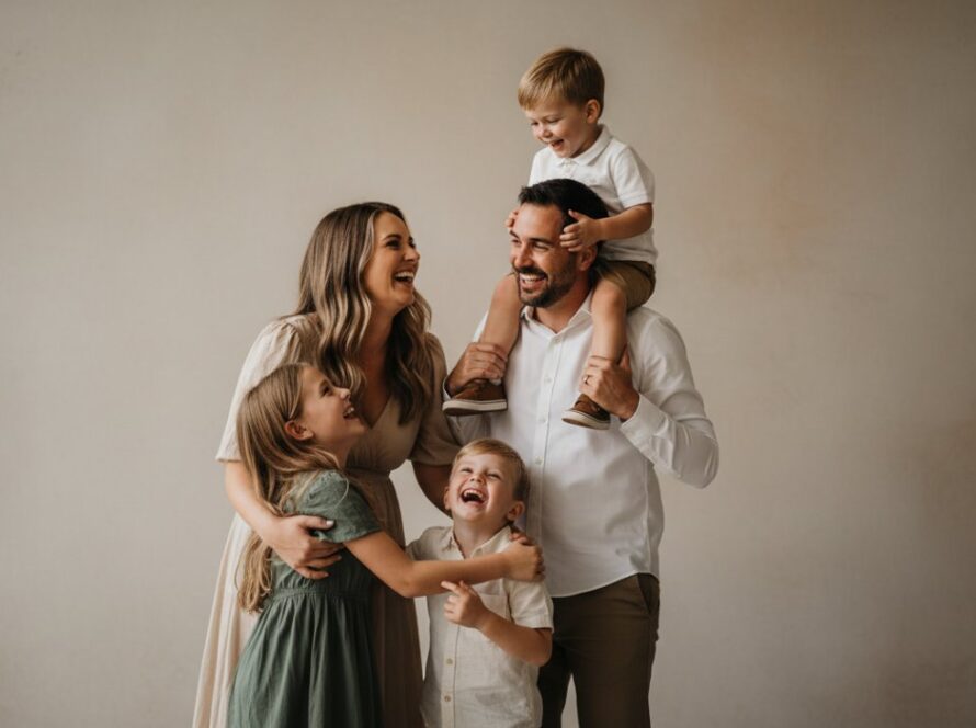 A vibrant family of four laughing joyfully during a bespoke studio photography session in Emerald, Victoria. The parents embrace their two young children, bathed in soft, professional lighting, capturing an authentic, 'epic moment' of connection. The image highlights the warm and inviting atmosphere of Emerald Victoria boutique studio photography for families.