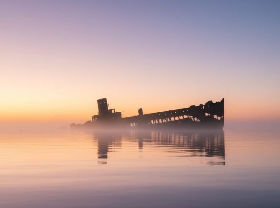 A dramatic, wide-angle 'epic moment' photograph showcasing the decaying iron structure of HMAS Cerberus historic shipwreck fine art photography, bathed in ethereal dawn light, with subtle waves crashing against its base and a lone pelican silhouetted against the sky, conveying a sense of timeless majesty and poignant history.