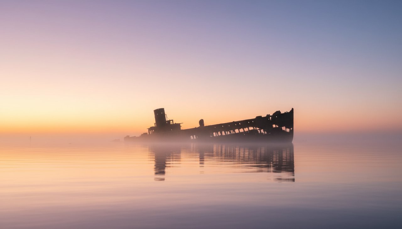 A dramatic, wide-angle 'epic moment' photograph showcasing the decaying iron structure of HMAS Cerberus historic shipwreck fine art photography, bathed in ethereal dawn light, with subtle waves crashing against its base and a lone pelican silhouetted against the sky, conveying a sense of timeless majesty and poignant history.