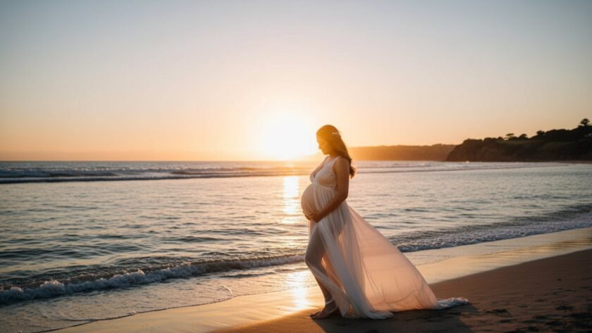 An expectant mother, silhouetted by a golden sunset over the tranquil waters of Daveys Bay, Mount Eliza, during her Mount Eliza coastal maternity photoshoot Victoria, her flowing dress catching the evening breeze.