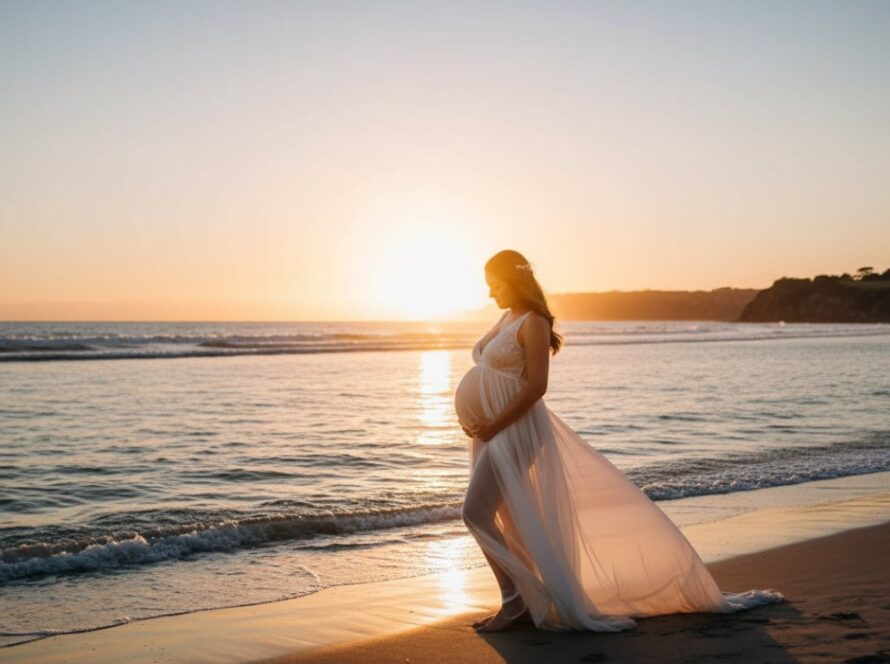 An expectant mother, silhouetted by a golden sunset over the tranquil waters of Daveys Bay, Mount Eliza, during her Mount Eliza coastal maternity photoshoot Victoria, her flowing dress catching the evening breeze.