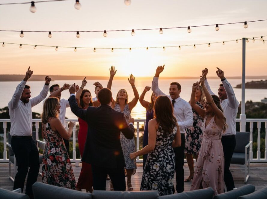 Vibrant Sorrento party photography capturing a joyous candid moment of guests dancing at a sunset celebration on a coastal venue balcony, with the sparkling ocean visible in the background.