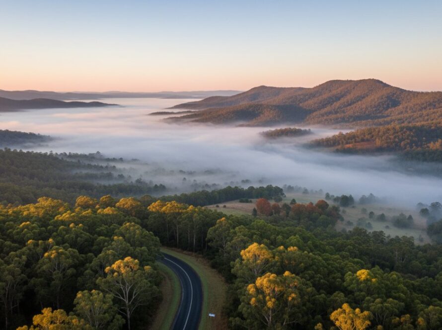A breathtaking aerial shot showcasing Upwey Victoria drone photography scenic views, with vibrant autumn foliage blanketing the Dandenong Ranges, early morning mist clinging to the valleys, and golden sunlight illuminating a winding road, capturing an epic moment of natural beauty.