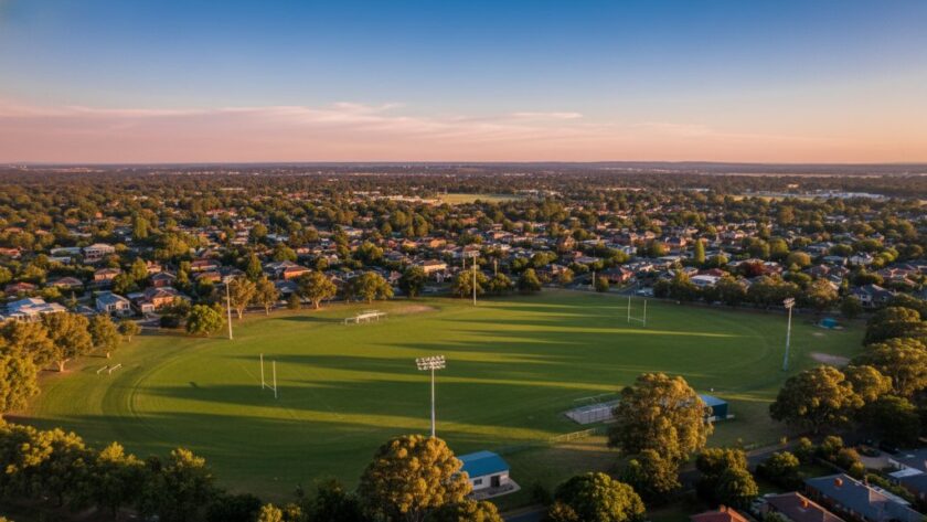 An epic moment of Alfredton Drone Photography Panoramic Views capturing the stunning, vibrant green cricket oval and historic red-brick buildings bathed in golden hour light, from a high aerial perspective, showcasing the expansive Victorian landscape.