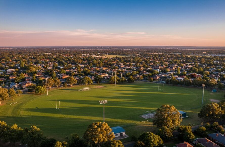 An epic moment of Alfredton Drone Photography Panoramic Views capturing the stunning, vibrant green cricket oval and historic red-brick buildings bathed in golden hour light, from a high aerial perspective, showcasing the expansive Victorian landscape.