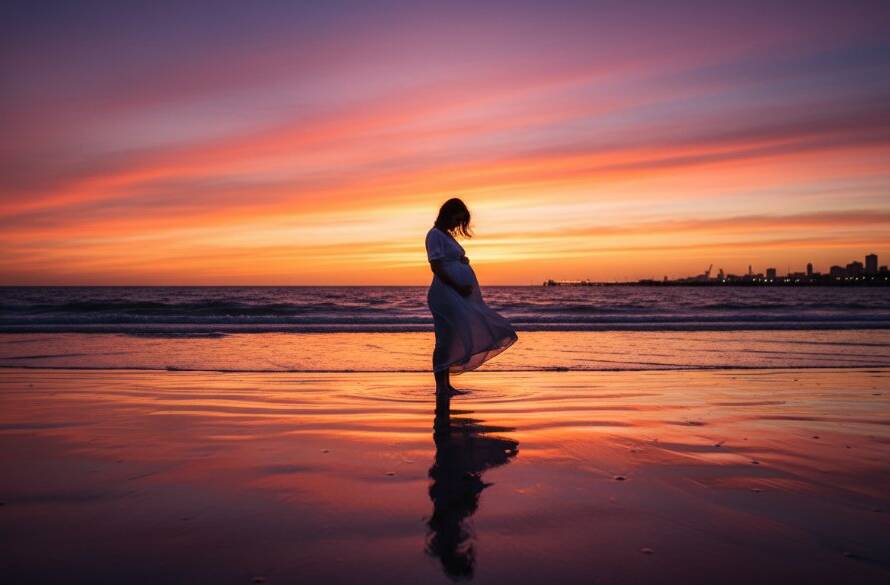 An awe-inspiring Altona beach golden hour maternity photoshoot moment, featuring a glowing pregnant woman silhouetted against a vibrant sunset, her hands cradling her bump, with gentle waves lapping the shore in the foreground, professional colour grading.