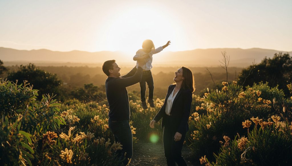 Authentic family photography Rowville Victoria capturing a joyous family moment at sunset, parents lifting their laughing child high, with the Dandenong Ranges in the soft focus background, professionally color-graded.
