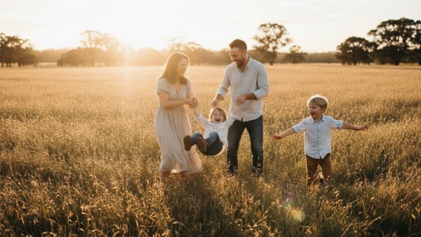 An authentic family photography Seymour Victoria portrait showing parents joyfully embracing their two young children amidst a golden hour field, backlit by the setting sun, evoking warmth and connection.