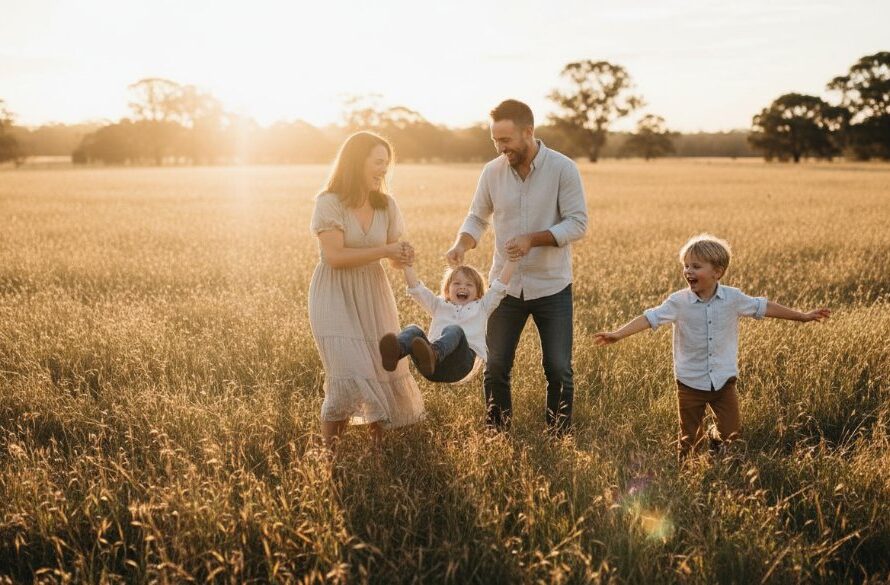 An authentic family photography Seymour Victoria portrait showing parents joyfully embracing their two young children amidst a golden hour field, backlit by the setting sun, evoking warmth and connection.