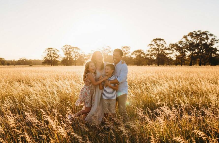 An epic moment capturing a family laughing joyfully during their authentic family photos Cranbourne West moments session, with warm evening light silhouetting them against a natural Cranbourne West parkland setting, showcasing genuine connection and happiness.