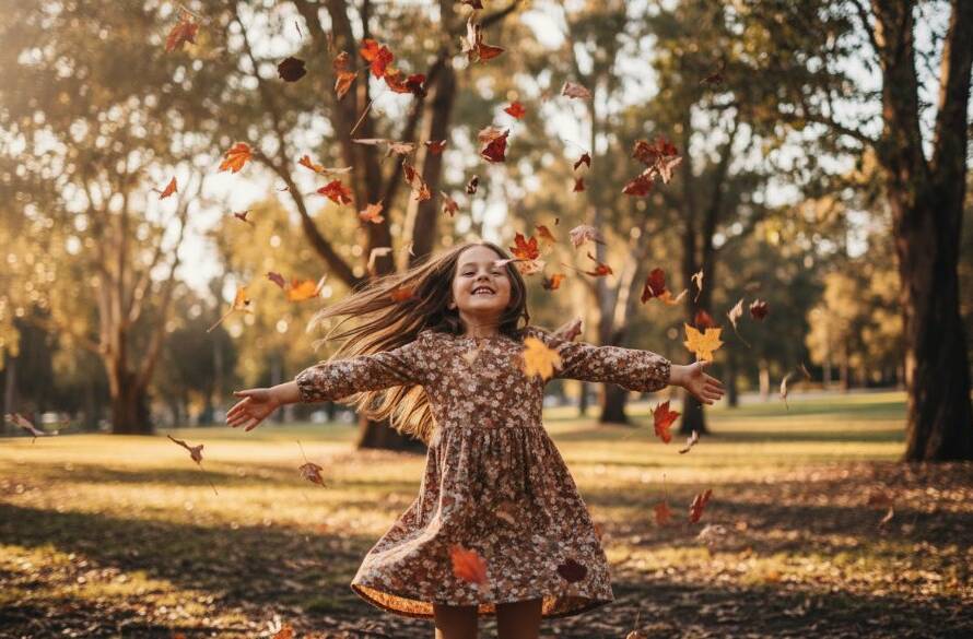 A wide-angle, cinematic photograph of a child (approx. 6-8 years old) running joyfully through a sun-drenched, leafy park in Croydon, Victoria, bathed in golden hour light, with a blurred background suggesting motion and freedom, embodying authentic kids photography Croydon Victoria.