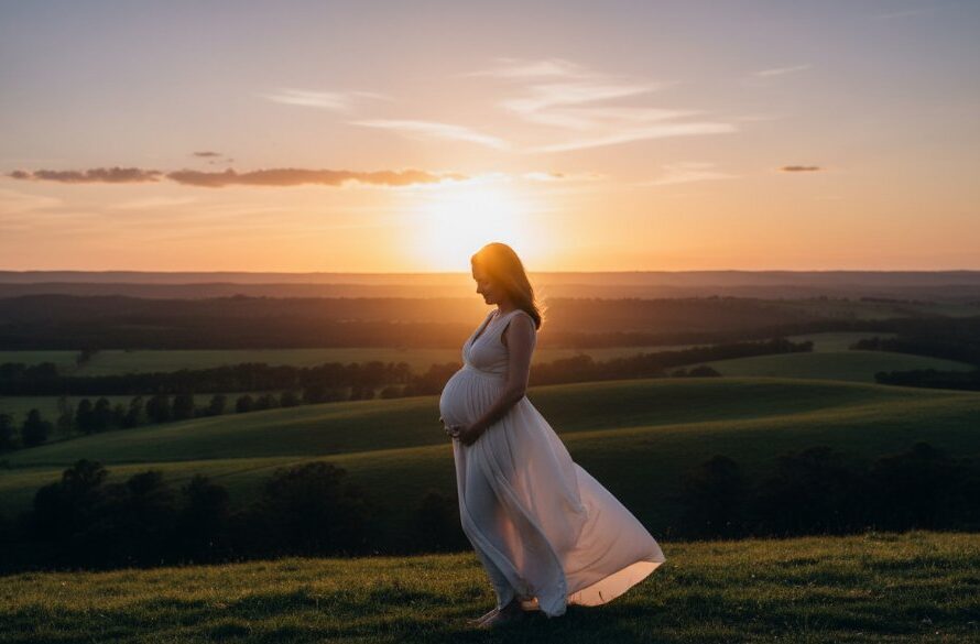 A radiant expectant mother, captured in authentic maternity photography Churchill Victoria, stands silhouetted against a dramatic sunset over rolling hills near Strzelecki Ranges, her hand gently cradling her belly, embodying a serene and powerful moment.