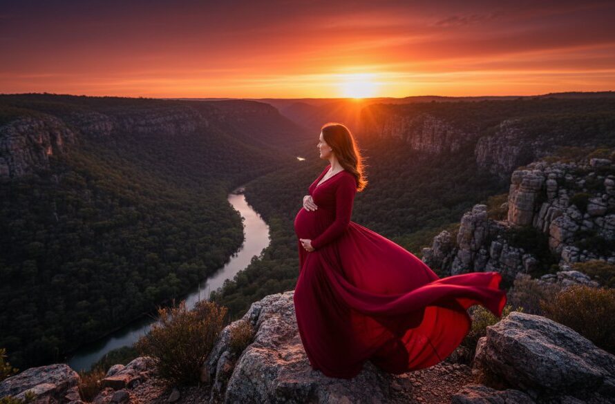 A radiant expectant mother in a flowing golden gown stands silhouetted against a breathtaking Bacchus Marsh sunset over the Lerderderg Gorge, her hands cradling her belly. The dramatic light and vibrant colours highlight the stunning Bacchus Marsh maternity photoshoot scenic locations, creating an epic, professional portfolio image.