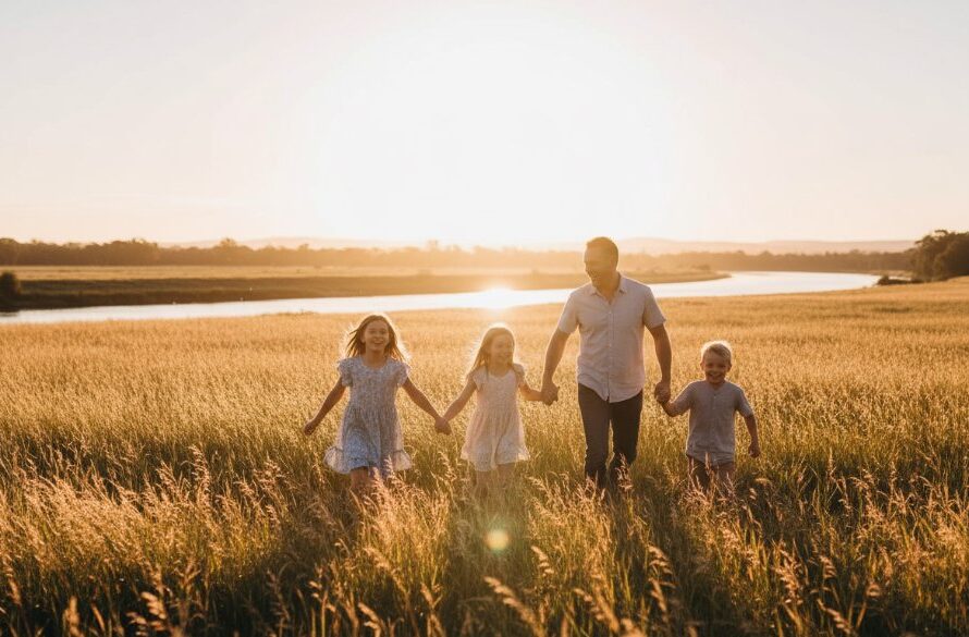 A joyful Bairnsdale outdoor family portraits capturing genuine emotion, with parents and two children laughing and running through sun-dappled fields near the Mitchell River, showcasing professional photography with dramatic golden hour lighting.