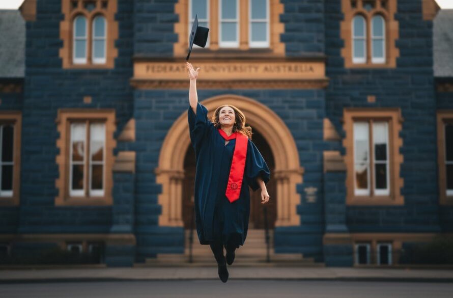 A joyous Ballarat Central graduation photography celebration portraits moment, featuring a graduate in full regalia triumphantly throwing their cap in front of the historic University of Ballarat building, bathed in golden hour light.