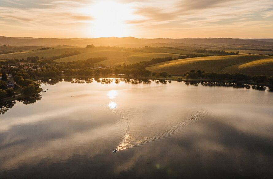 An epic aerial shot from a Benalla drone photography session capturing rural Victoria landscapes, featuring a golden sunset over Lake Benalla with rolling hills in the background and a lone kayaker. The scene is bathed in warm, dramatic light, showcasing the serene beauty of the region.