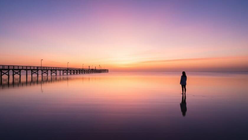An epic, dramatically lit fine art photograph capturing the serene beauty of Bonbeach fine art coastal photography at sunrise, with a lone figure contemplating the calm, golden-hour bay.
