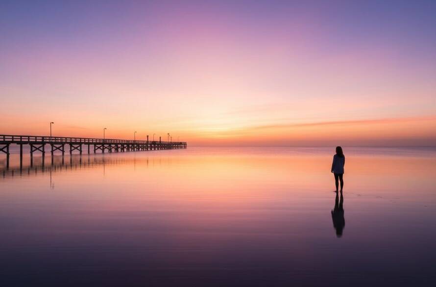 An epic, dramatically lit fine art photograph capturing the serene beauty of Bonbeach fine art coastal photography at sunrise, with a lone figure contemplating the calm, golden-hour bay.