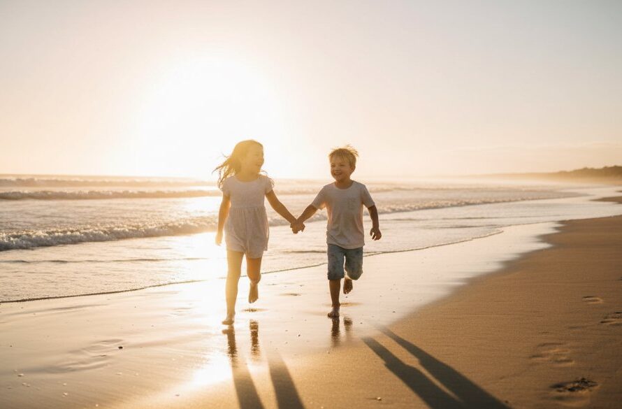 An epic moment of pure joy captured during a candid family moments Wonthaggi kids photography session, featuring two children laughing as they chase waves on the sun-drenched Wonthaggi beach at sunset, with dramatic golden light, professionally colour-graded.