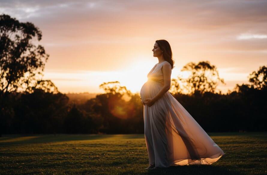 A glowing pregnant woman in a flowing white gown stands amidst the golden hour light of a Heathmont park, her partner gently embracing her from behind. This candid Heathmont outdoor maternity photos Victoria capture an epic moment of connection and anticipation, with dramatic backlighting and professional colour grading, embodying the joy of impending parenthood.