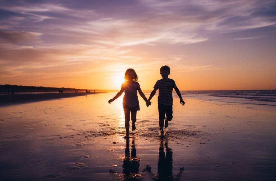 An epic moment of genuine joy captured during candid kids photography Carrum beach sunsets, showing two children laughing and running on the sandy shore with golden light reflecting on the water at dusk, a professional, color-graded photograph.