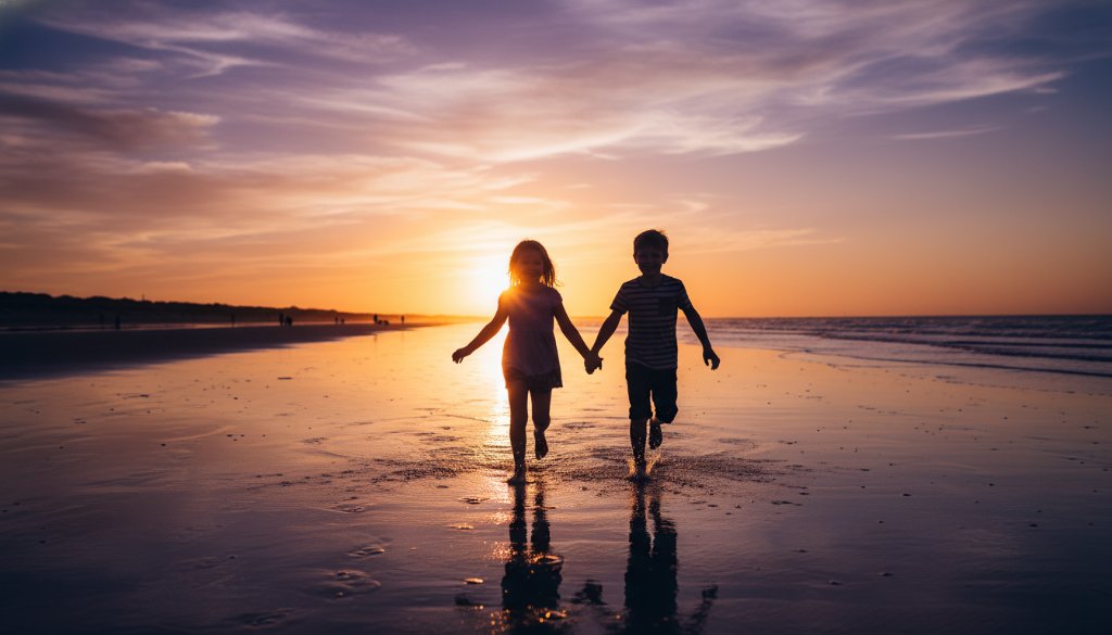 An epic moment of genuine joy captured during candid kids photography Carrum beach sunsets, showing two children laughing and running on the sandy shore with golden light reflecting on the water at dusk, a professional, color-graded photograph.