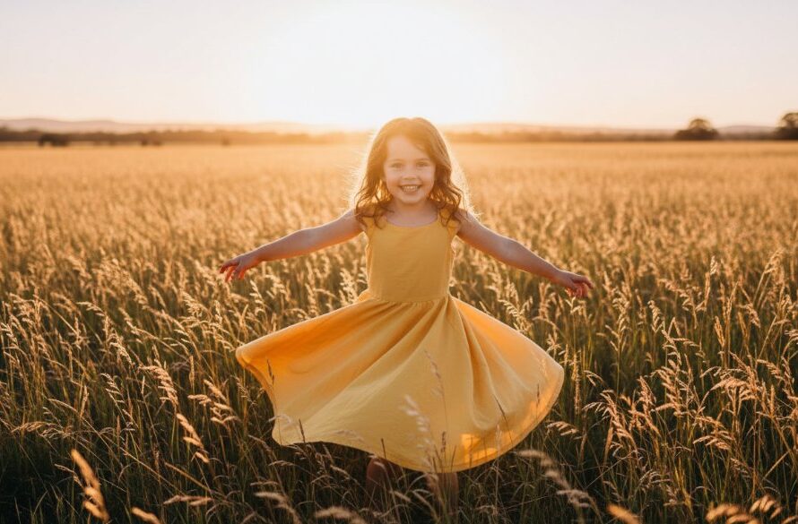 An epic moment captured in Newborough, featuring a young child laughing joyfully as they run through a field of golden grass at sunset, their parents silhouetted softly in the background. The candid kids photography Newborough family portraits image highlights the child's pure delight, with dramatic backlight creating a golden halo and professional cinematic colour grading.