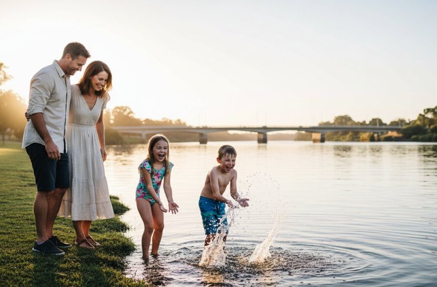 A wide shot capturing authentic candid moments Bairnsdale, featuring a family laughing joyfully by the Mitchell River, with the evening sun casting a warm glow and the Bairnsdale bridge visible in the background, showcasing genuine connection and professional colour grading.