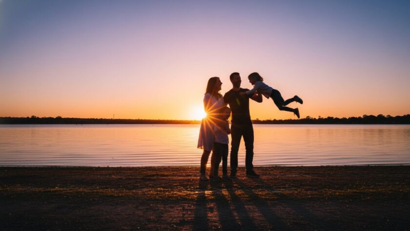 A stunning candid photograph 'Capturing candid family joy Maryborough Victoria', showing a family laughing heartily on a golden-lit afternoon near Lake Victoria in Maryborough, silhouetted slightly with warm, cinematic tones.