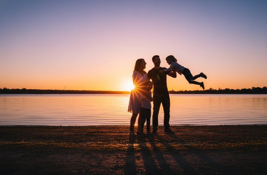 A stunning candid photograph 'Capturing candid family joy Maryborough Victoria', showing a family laughing heartily on a golden-lit afternoon near Lake Victoria in Maryborough, silhouetted slightly with warm, cinematic tones.