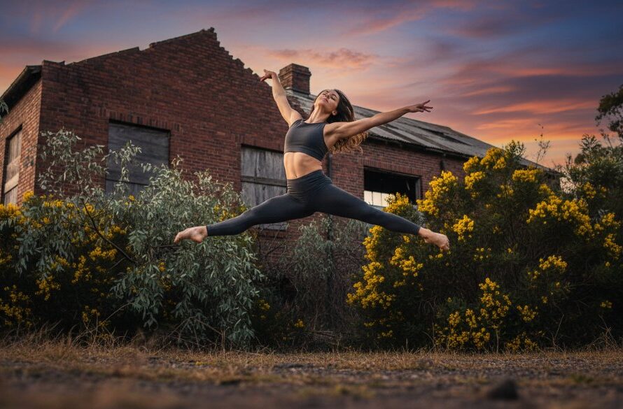 A male dancer in mid-air, performing a powerful leap against a soft-focus industrial backdrop in Morwell, Victoria, showcasing capturing dynamic dance photography Morwell Victoria with dramatic lighting and strong composition.
