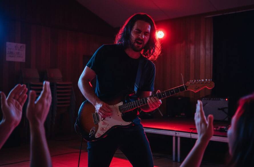 An electrifying wide shot capturing electrifying Koo Wee Rup live music moments at a local venue, with a lead guitarist in mid-solo, stage lights flaring, and the crowd silhouetted against vibrant colours, conveying the raw energy of a performance.