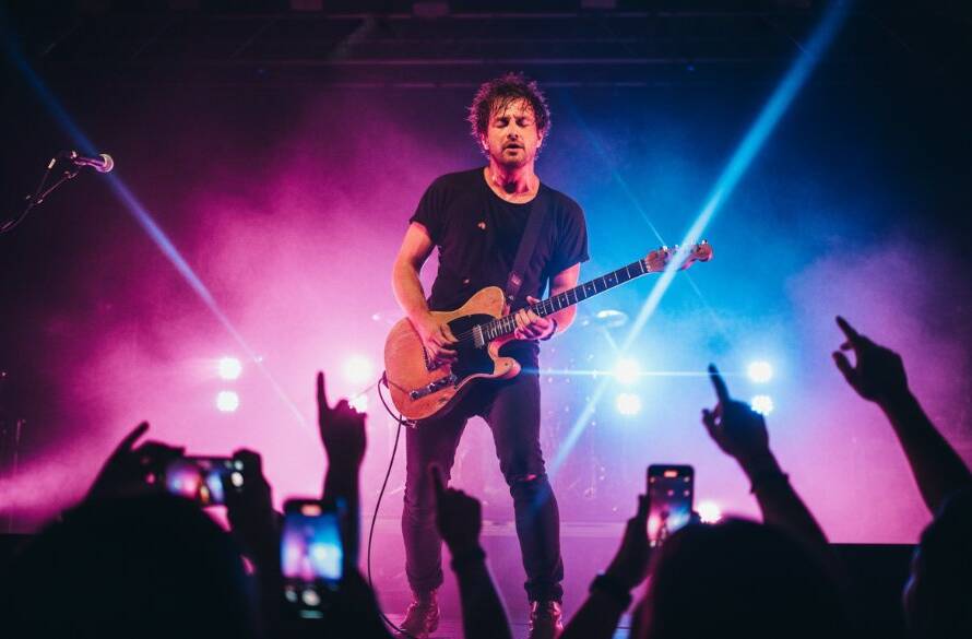 A dynamic shot of a lead guitarist mid-shred, bathed in vibrant stage lights, capturing electrifying live music moments Sunshine West, with the crowd's energy palpable in the foreground.