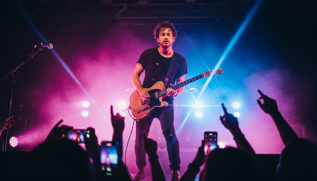 A dynamic shot of a lead guitarist mid-shred, bathed in vibrant stage lights, capturing electrifying live music moments Sunshine West, with the crowd's energy palpable in the foreground.