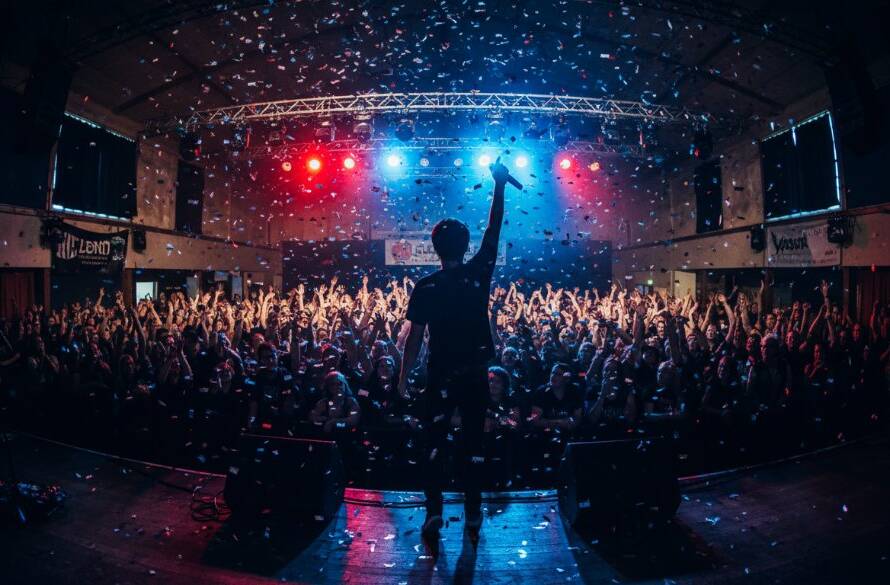 Dramatic, high-energy photograph capturing live music Croydon South Victoria, showcasing a lead guitarist mid-shred under intense stage lights, with blurred audience hands in the foreground, conveying the electric atmosphere of a local concert.