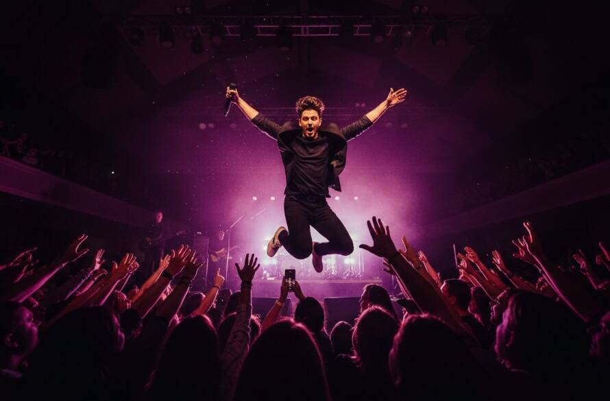 An electrifying wide-angle shot from the front row at a Mitcham gig, capturing live music energy with a lead guitarist mid-shred, bathed in dramatic red and blue stage lights, sweat flying, against a blurred backdrop of an excited crowd, showcasing an epic moment of raw performance.