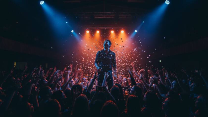 A dynamic, wide-angle shot of a lead guitarist mid-shred, bathed in dramatic magenta and blue stage lights at a vibrant local venue in Ringwood North, capturing Ringwood North live music energy. The crowd's silhouettes are visible, hands raised, creating an epic moment of connection and raw musical passion, professionally colour-graded.