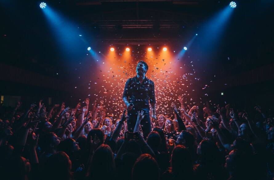 A dynamic, wide-angle shot of a lead guitarist mid-shred, bathed in dramatic magenta and blue stage lights at a vibrant local venue in Ringwood North, capturing Ringwood North live music energy. The crowd's silhouettes are visible, hands raised, creating an epic moment of connection and raw musical passion, professionally colour-graded.