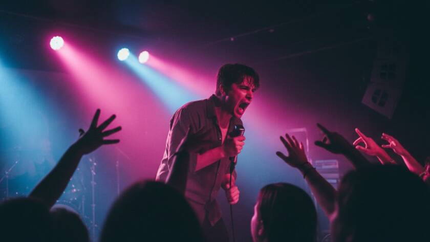 An epic shot Capturing Vibrant Live Music Photography Croydon North Victoria, featuring a lead singer mid-scream, bathed in dramatic magenta and blue stage lights, a blurred but energetic crowd in the foreground.