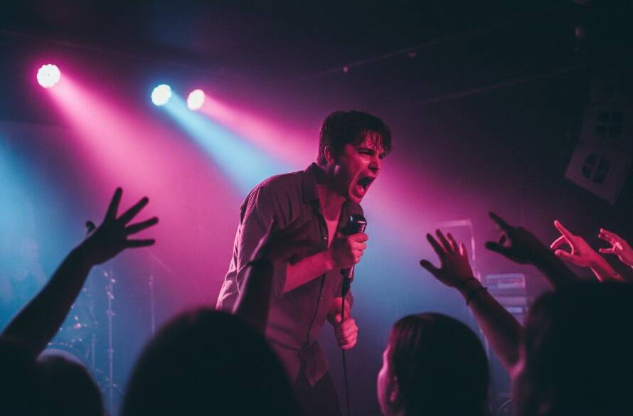 An epic shot Capturing Vibrant Live Music Photography Croydon North Victoria, featuring a lead singer mid-scream, bathed in dramatic magenta and blue stage lights, a blurred but energetic crowd in the foreground.