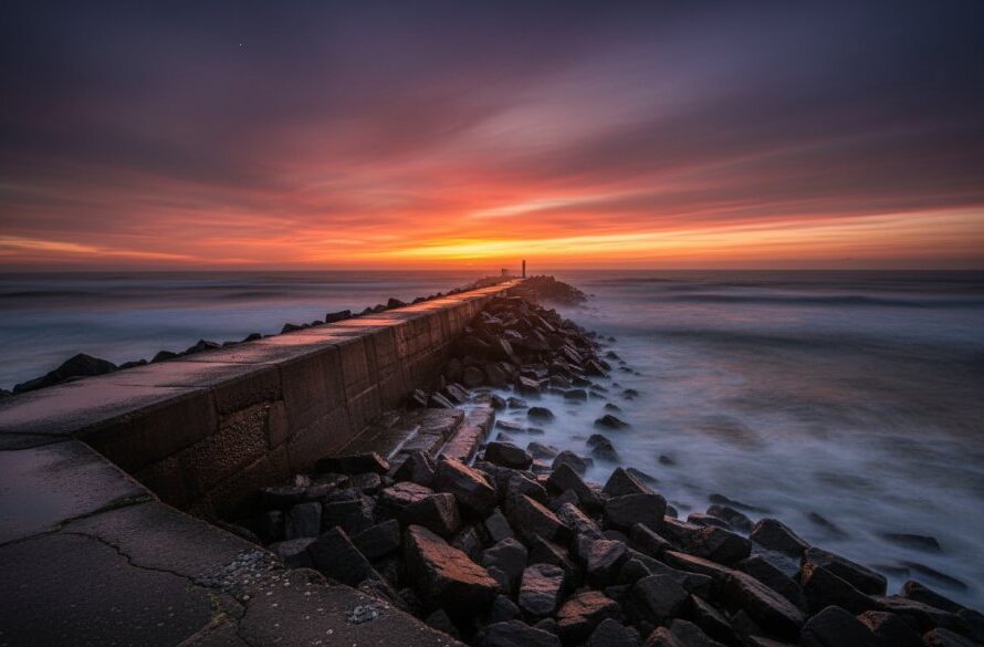 A dramatic long exposure photograph of the iconic Warrnambool Breakwater at dawn, with golden light illuminating its historic stone structure and the wild Southern Ocean waves crashing around it, perfectly Capturing Warrnambool's historic architecture photography with a sense of timeless grandeur and resilience.