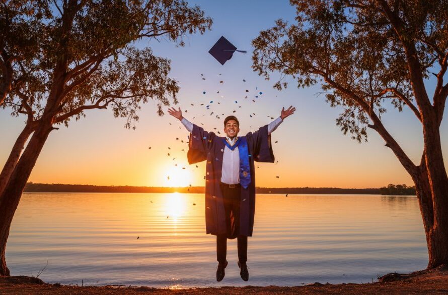 A jubilant graduate in their cap and gown, framed against the stunning sunset over Lake Mulwala, celebrating their achievement, perfectly embodying capturing Yarrawonga graduation joy photography.