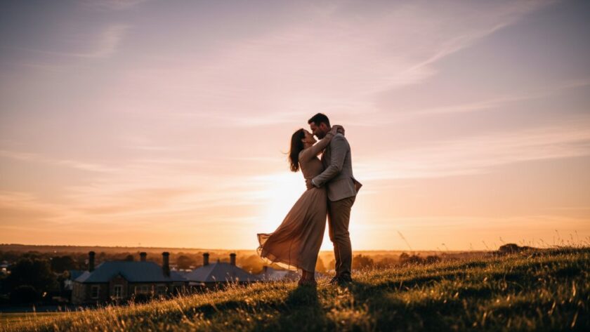An engaged couple embraces passionately on a hilltop overlooking Castlemaine at sunset, with golden light illuminating their joyful expressions, expertly showcasing Castlemaine engagement photography capturing sunset magic.