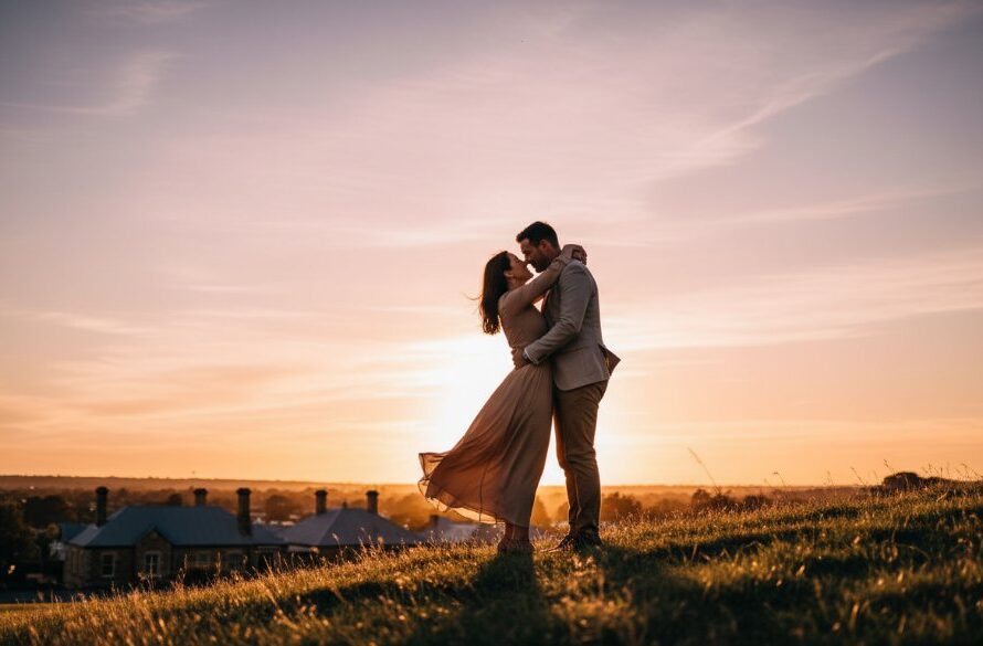 An engaged couple embraces passionately on a hilltop overlooking Castlemaine at sunset, with golden light illuminating their joyful expressions, expertly showcasing Castlemaine engagement photography capturing sunset magic.