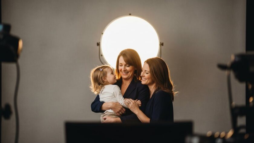 An emotionally resonant, wide-angle, professional photograph showcasing a family of three (parents and a young child) bathed in soft, warm studio light, laughing genuinely. The focus is on their joyous connection, captured in a Colac boutique studio photography for timeless portraits session, with a subtle, elegant backdrop and cinematic colour grading.