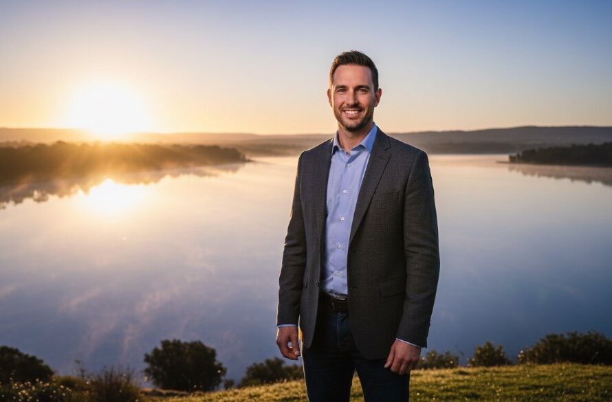 A dramatic, cinematic headshot of a confident female entrepreneur in Colac, standing near the tranquil shores of Lake Colac at sunset. The 'Colac Professional Headshots for Local Business Growth' image features a warm, golden hour glow highlighting her determined expression, with the iconic Colac Botanic Gardens subtly blurred in the background, conveying professionalism and local connection.