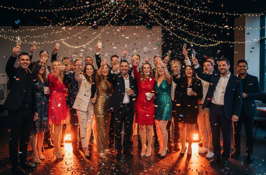 Dramatic wide shot of an indoor birthday party in Dandenong South, Victoria, showcasing a vibrant moment of guests toasting with joy, expertly captured through Dandenong South party photography unforgettable celebrations, with professional lighting and rich colours.